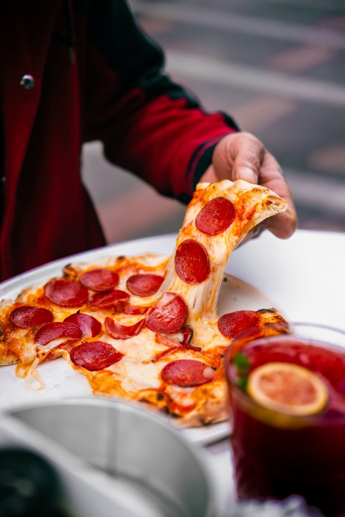 Close-up of a hand pulling a cheesy pepperoni pizza slice, perfect for food lovers.